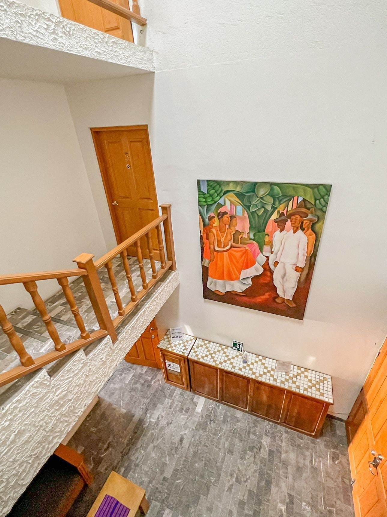 Interior d'hotel amb diversos nivells, una escala, una porta de fusta, un taulell de quadres i un quadre a la paret.