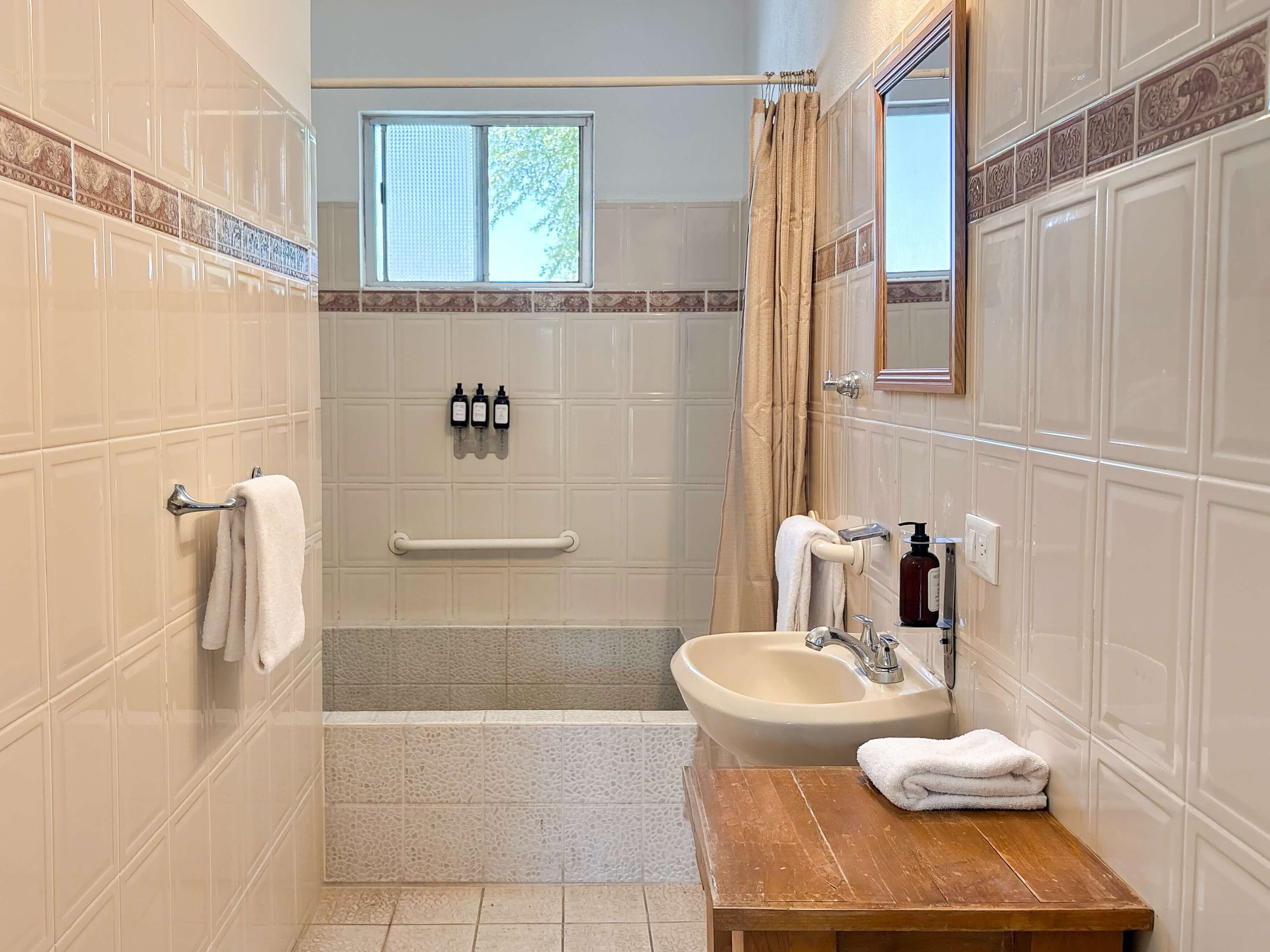 Un baño con una bañera, un lavabo, un tocador de madera, un perchero para toallas, una ventana y un espejo.
