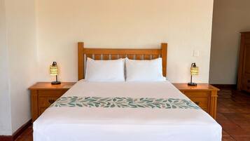 Una cama bien hecha con sábanas blancas y una colcha de estampado floral, flanqueada por mesitas de noche de madera con lámparas.