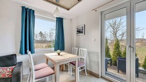 A room with a dining table, chairs, a sofa, a ceiling light, a window with curtains, and a view of the outdoors.