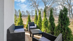 An outdoor patio with wicker furniture and a view of a fenced area with trees.