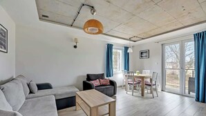 Un salon moderne comprenant un canapé, une table basse, une table à manger avec des chaises et une grande fenêtre avec des rideaux.