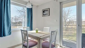 Un espace repas comprenant une table, des chaises, un luminaire suspendu et une vue à travers une porte vitrée.