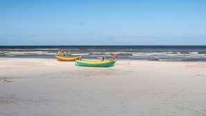 Une plage avec deux bateaux sur le sable, un ciel dégagé et l’océan en arrière-plan.