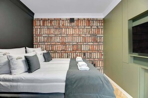 Ein Hotelzimmer mit einer Wand im Ziegelsteinmuster, einem Bett mit weißer Bettwäsche und einem an der Wand montierten Fernseher.