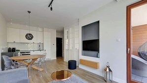 A modern kitchen with white cabinets, a wooden dining table, and a large TV mounted on the wall. - Gdynia Orłowo | 450 metres to the Beach (Gdynia)