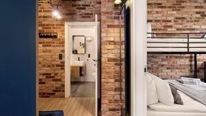 Een kamer met een stapelbed, een bakstenen muur, een houten vloer, een witte wasbak en een spiegel.