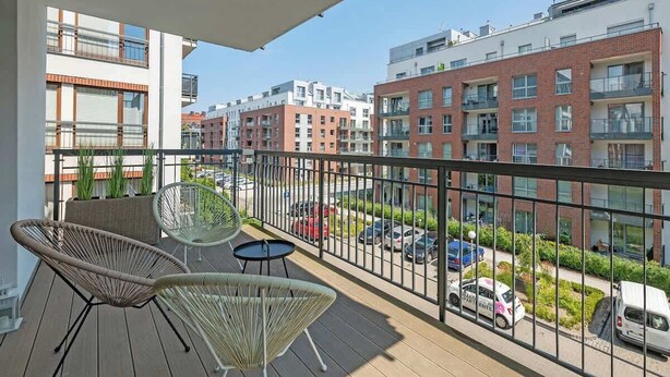 A balcony with wicker chairs and a table, overlooking a street with parked cars and buildings. - Szafarnia 9B | Next to Marina | 2 Parking spots (Gdańsk)
