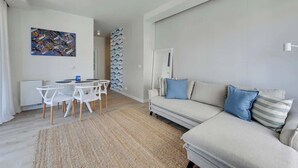 A modern living room with a sofa, a dining table with chairs, a rug, and a painting on the wall. - Szafarnia 9B | Next to Marina | 2 Parking spots (Gdańsk)
