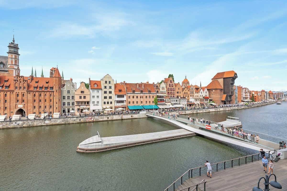 A riverside promenade with historic buildings, a bridge, and a waterfront view.