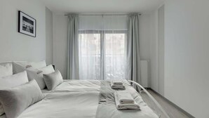 Una moderna camera d'albergo con un letto rifatto, un comodino e una finestra con tende leggere.