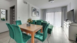Un soggiorno moderno con zona pranzo, TV a schermo piatto e un'ampia finestra con tende.