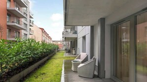 Un appartement moderne doté d’un balcon, d’un petit jardin et d’un coin salon avec deux fauteuils.