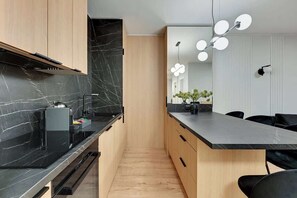 A modern kitchen with black marble countertops, wooden cabinets, and a central island with a black countertop. - Grano Residence 2 | Riverside | Parking (Gdańsk)