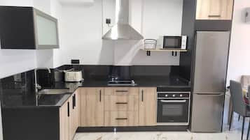 A modern kitchen with black countertops, wooden cabinets, a stainless steel range hood, a microwave, a toaster, and a refrigerator.