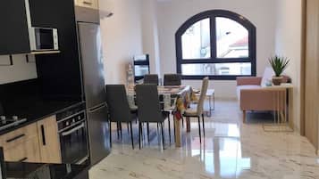 A modern kitchen with black cabinetry, a built-in microwave, and a stainless steel refrigerator. There is a dining area with a table and chairs, and a large arched window providing natural light.