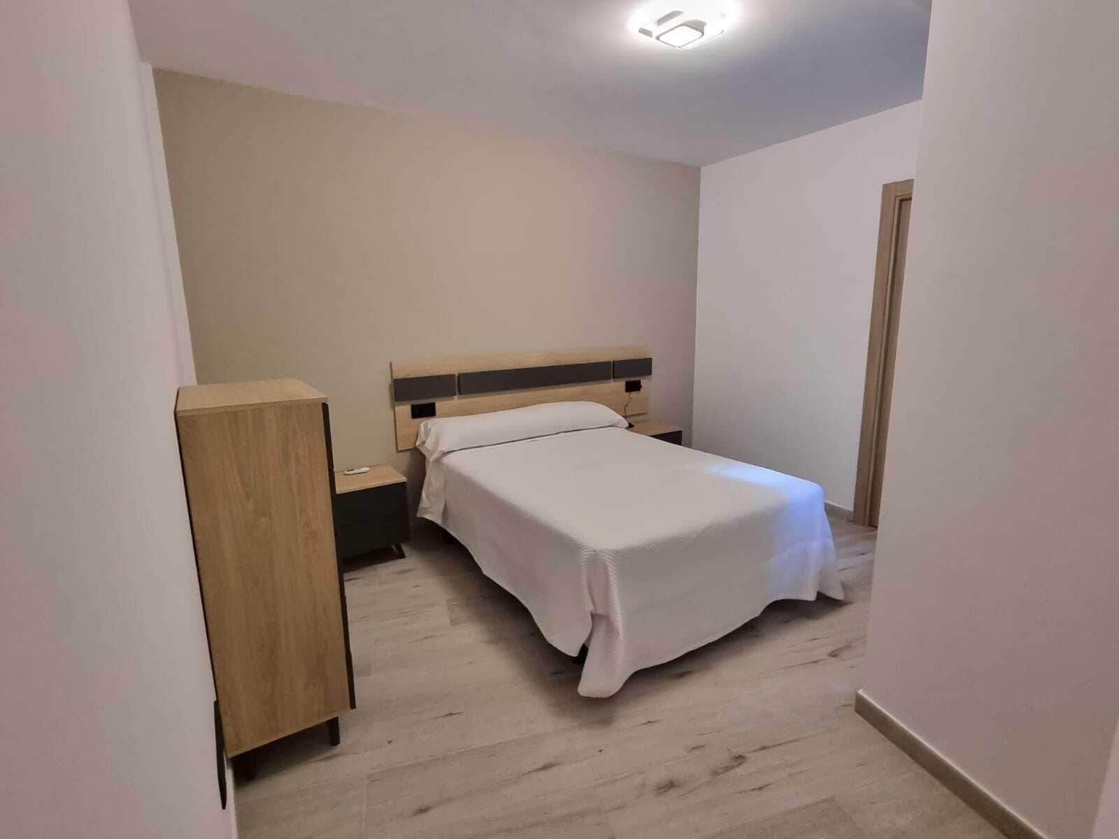 A small, neatly arranged bedroom with a single bed, a nightstand, and a wooden wardrobe.