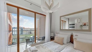 A hotel room with a large bed, a balcony with a view of buildings, a large mirror, and a hanging light fixture. - Aura 196A | River View | City Centre & Parking (Gdańsk)