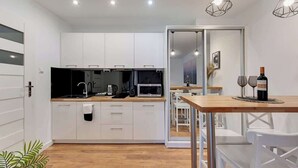 A modern kitchen with white cabinets, a microwave, and a dining area with a wooden table and white chairs. - Aura 196A | River View | City Centre & Parking (Gdańsk)