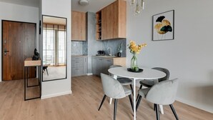 A modern kitchen with wooden cabinets, a round dining table with chairs, and a vase of flowers. - Brabank 17 | Riverside & Balcony | Parking (Gdańsk)