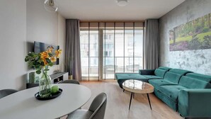 A modern living room with a sofa, a dining table, and a TV. - Brabank 17 | Riverside & Balcony | Parking (Gdańsk)