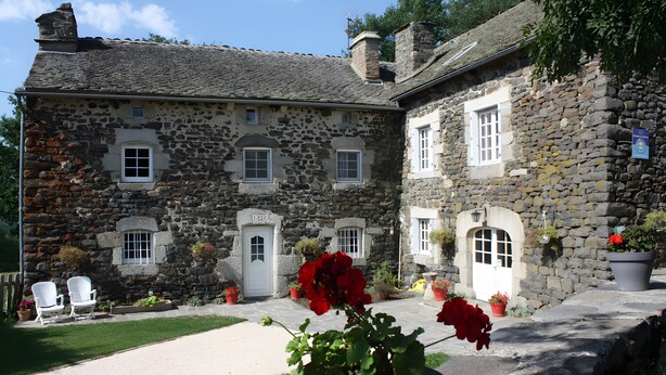 Un bâtiment en pierre avec une porte blanche, des fenêtres et une cour dallée.