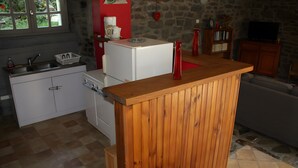 Une cuisine avec un comptoir en bois, un réfrigérateur, un évier et un mur en pierre.