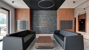 Rebedor modern amb dos sofàs negres, una taula de centre de fusta i una paret de marbre amb un logotip.
