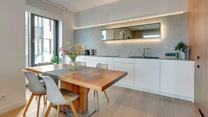 A modern kitchen with a wooden dining table, white cabinets, and a large window. - Brabank 26 | Riverside & Balcony | Parking (Gdańsk)