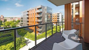 A balcony with a view of modern buildings, a wooden floor, and white furniture. - Brabank 26 | Riverside & Balcony | Parking (Gdańsk)