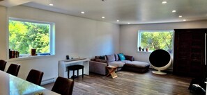 A modern living room with a sofa, a round black chair, a dining table with chairs, and a piano. - Bright Modern Open Haven with Tree-Lined Terrace (Montréal)