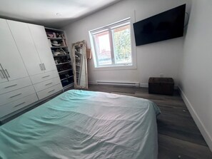 A bedroom with a bed, wardrobe, mirror, window, and a television on the wall. - Bright Modern Open Haven with Tree-Lined Terrace (Montréal)