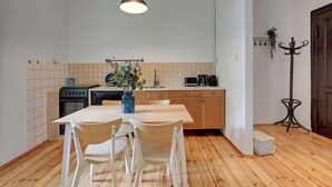 Et lille køkken med spisebord, stole, en hængende lampe og et knagered.