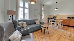 En moderne stue med en grå sofa, et lille rundt bord og et køkken med træskabe og et spisebord.
