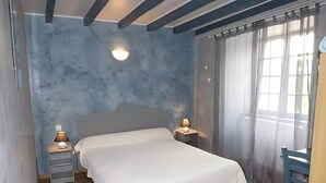 A bedroom with a bed, bedside lamps, a nightstand, a chair, and a window with curtains.