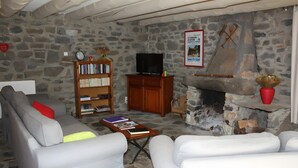 A stone-walled room with a fireplace, a television, a bookshelf, and a sofa.
