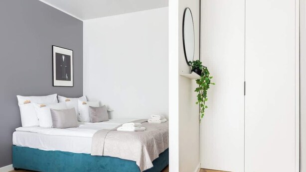 A bedroom with a bed, pillows, a bedside table, a framed picture, a mirror, and a potted plant. - Angielska Grobla 82B | Near Old Town & Marina (Gdańsk)