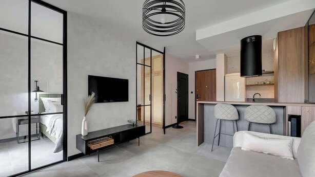 Een modern interieur met een bank, een houten bijzettafeltje en een aan de muur bevestigde televisie.
