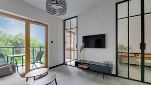 Een moderne woonkamer met een bank, een salontafel, een aan de muur bevestigde televisie, een schuifpui naar een balkon en een kleine bijzettafel.