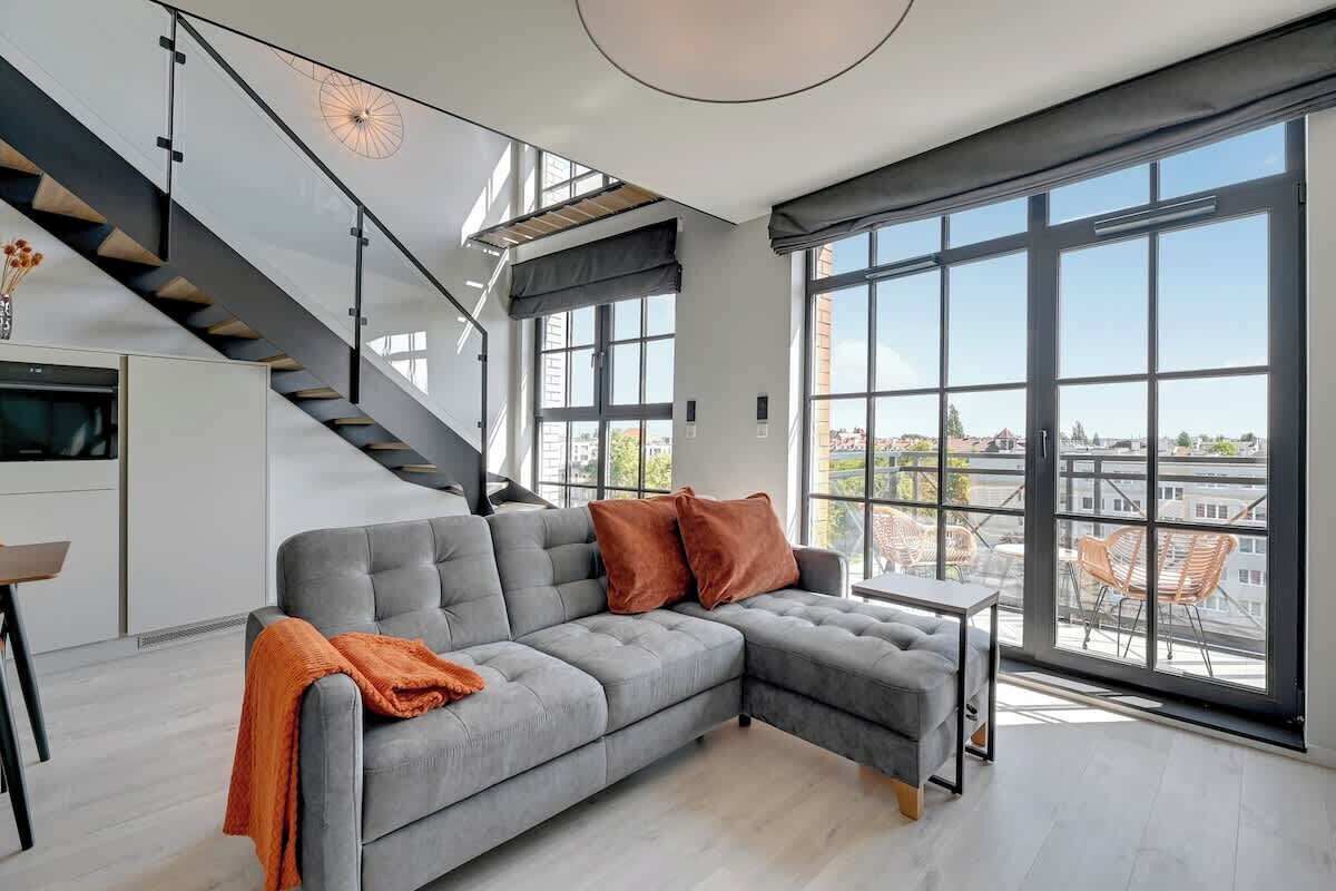 Ein modernes Wohnzimmer mit einem grauen Ecksofa, einem kleinen Tisch und einer Treppe.