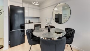 Una cocina moderna con un refrigerador negro, armarios blancos, una mesa redonda de comedor con sillas negras y un espejo grande en la pared.