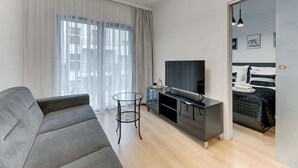 Una sala de estar moderna con un sofá, un televisor, una mesita y una cama con cubrecama a rayas.