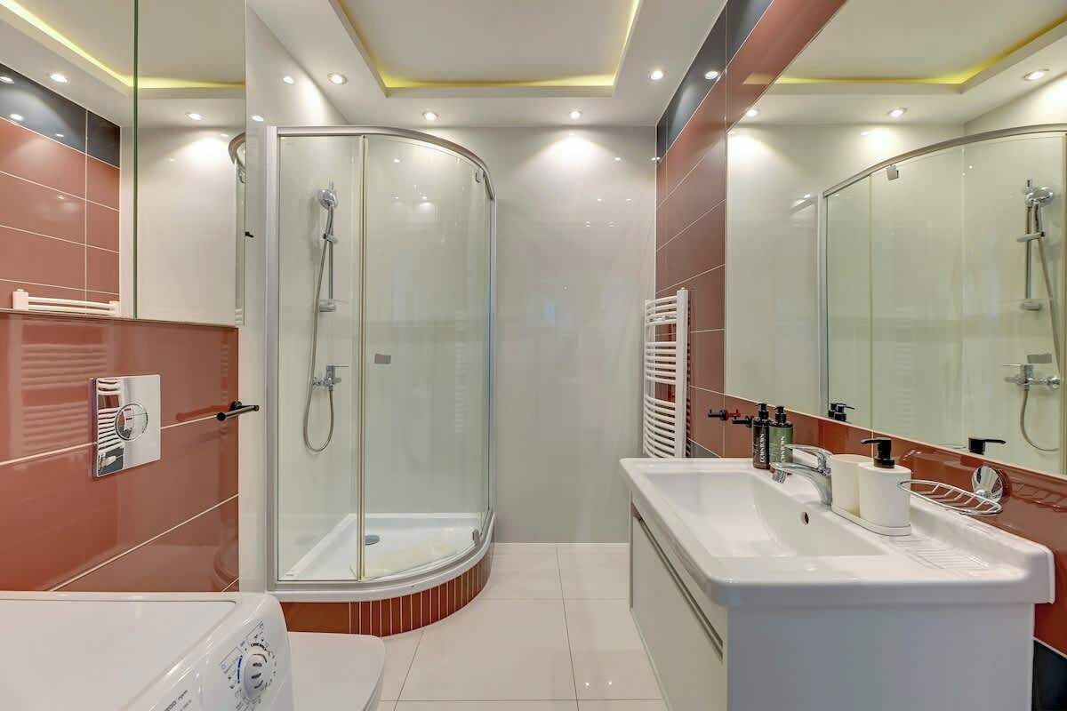 Een moderne badkamer met een douche in een glazen cabine, een wit wastafelmeubel en een grote spiegel.