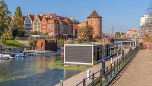 A riverside view with historic buildings, a tower, and a modern structure near the water.