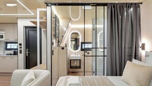 A modern hotel room with a bed, a seating area, a vanity, and a kitchenette.