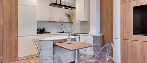 Una cocina moderna con armarios blancos, una mesa de comedor de madera y sillas transparentes.