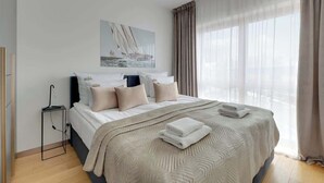 Een slaapkamer met een bed, nachtkastje, schilderij, raam met gordijnen en uitzicht.