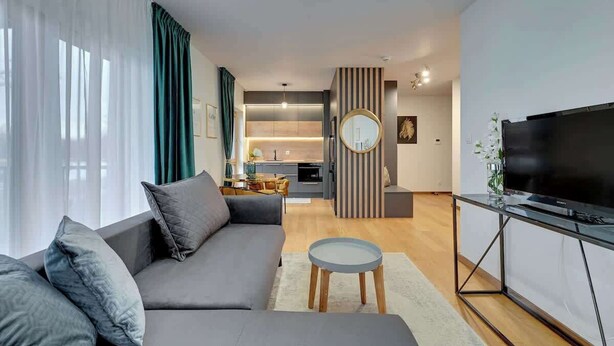 Een moderne woonkamer met een bank, een televisie en een keuken op de achtergrond.