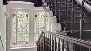 Una escalera con barandillas oscuras y pasamanos, que lleva a un rellano con una puerta blanca y un vitral.