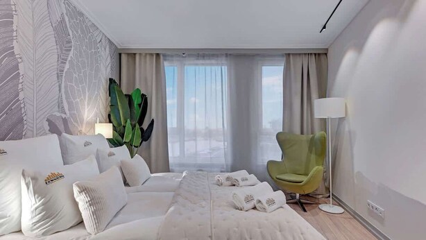 Ein Hotelzimmer mit einem Bett, einem grünen Sessel, einer großen Pflanze und Blick auf die Stadt.